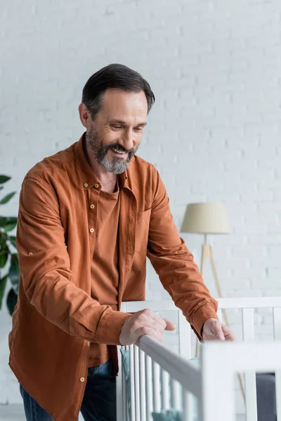 Positive man standing near blurred baby crib at home — Stock Photo