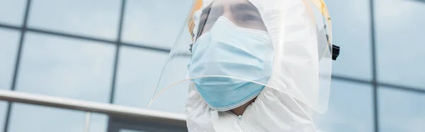 Low angle view of medical worker in visor and protective mask outdoors, banner — Stock Photo