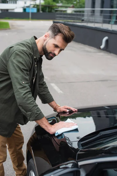 Jovem em roupas casuais limpando carro ao ar livre — Fotografia de Stock