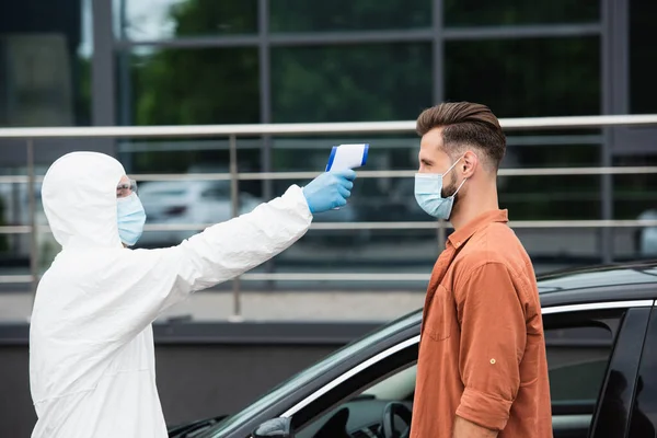 Motorista em máscara de pé perto do trabalhador médico com pirômetro e carro — Fotografia de Stock