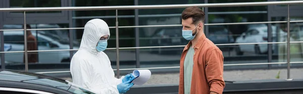 Medical worker writing on clipboard near driver and car outdoors, banner — Stock Photo
