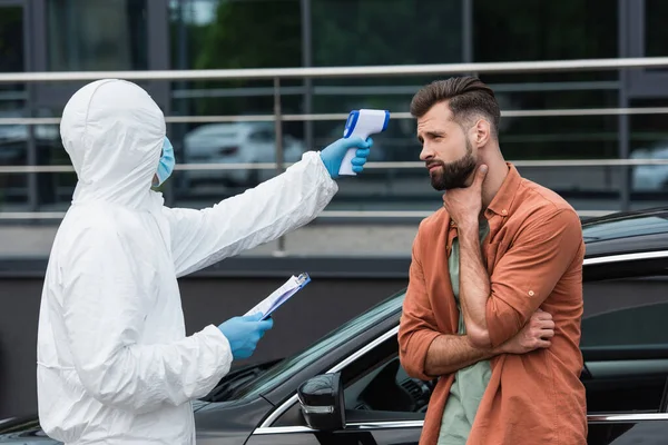 Medical worker checking temperature of sick driver near car outdoors — Stock Photo