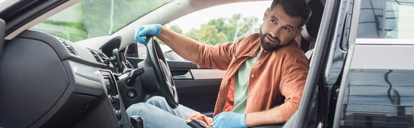 Бородатий водій в латексних рукавичках дивиться в авто, банер — стокове фото