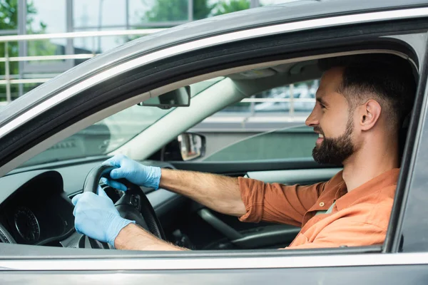 Вид сбоку улыбающегося водителя в латексных перчатках за рулем автомобиля — стоковое фото