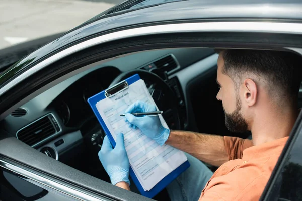 Seitenansicht des Fahrers in Latexhandschuhen, Schrift auf Klemmbrett im Auto — Stockfoto