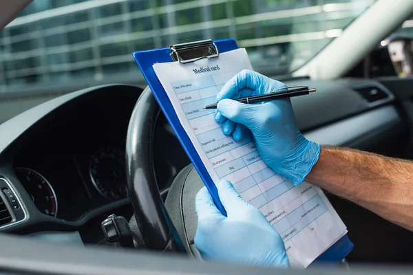 Cropped view of driver in latex gloves writing on medical card in auto — Stock Photo