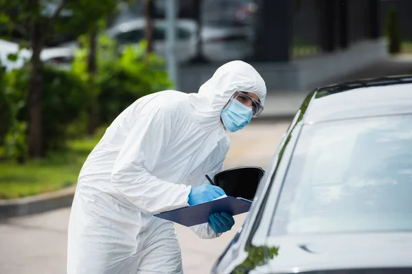 Border guard in medical mask with clipboard looking through car on blurred foreground — Stock Photo