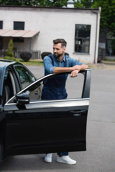 Mécanicien en salopette debout près de la porte ouverte de la voiture — Photo de stock