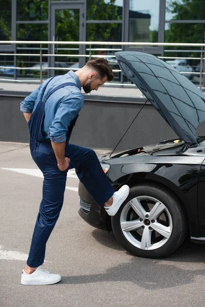 Side view of mechanic in overalls checking wheel of car outdoors — Stock Photo