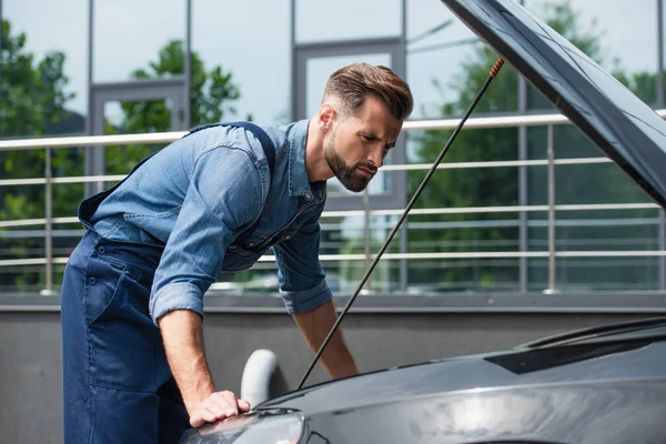 Pensive mechanic стоїть біля автомобіля з відкритим капюшоном — стокове фото