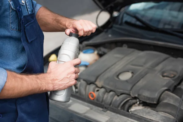 Cropped view of mechanic in uniform holding bottle of motor oil near blurred car — Stock Photo