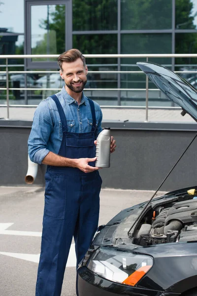 Sourire mécanicien tenant bouteille d'huile moteur près de la voiture à l'extérieur — Photo de stock