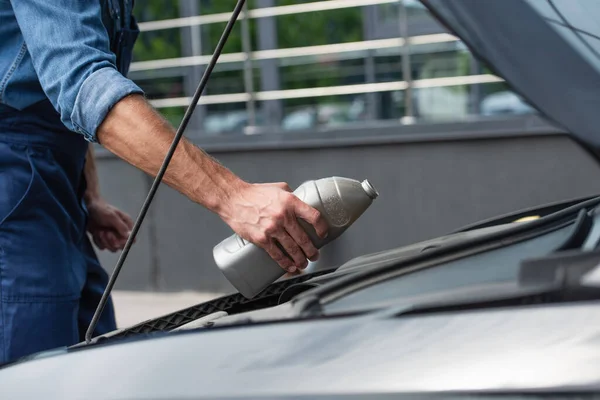 Cropped view of mechanic holding motor oil near car with open hood — Stock Photo