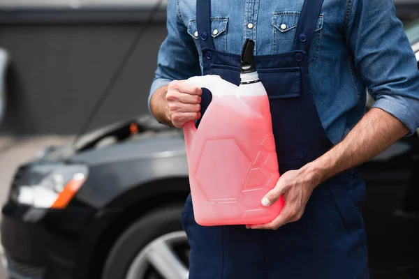 Vista ritagliata del riparatore che tiene il liquido della rondella del parabrezza vicino auto offuscata — Foto stock