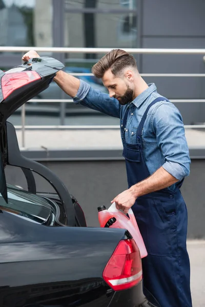 Seitenansicht des Mechanikers hält Scheibenwaschflüssigkeit und öffnet Motorhaube des Autos — Stockfoto