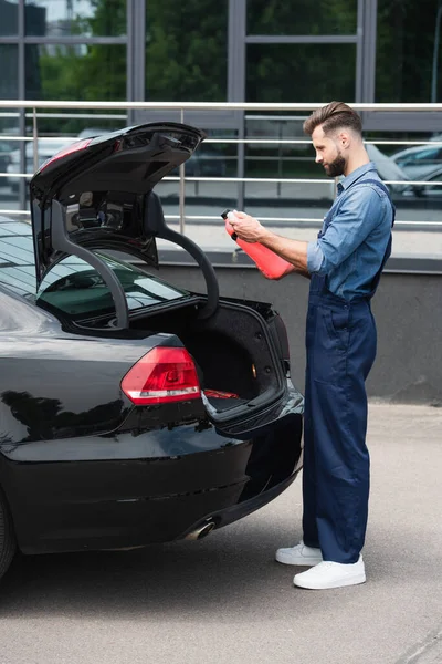 Seitenansicht des Mechanikers mit Blick auf Kanister mit Scheibenwaschflüssigkeit in der Nähe des Autos — Stockfoto