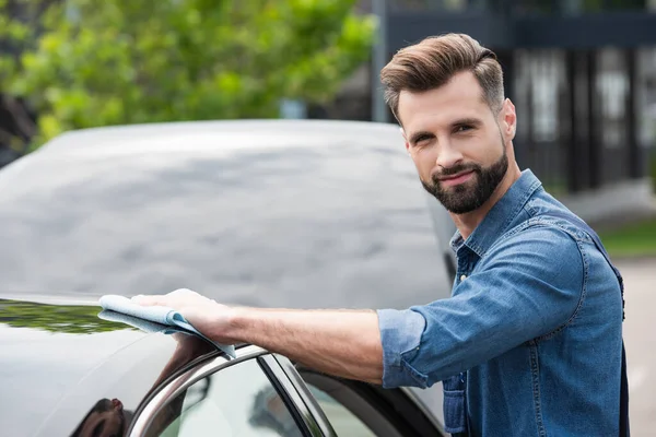 Mécanicien regardant la caméra tout en cire voiture avec chiffon à l'extérieur — Photo de stock