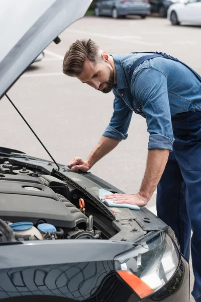 Mechaniker hält Lappen und reinigt Auto mit offener Motorhaube im Freien — Stockfoto