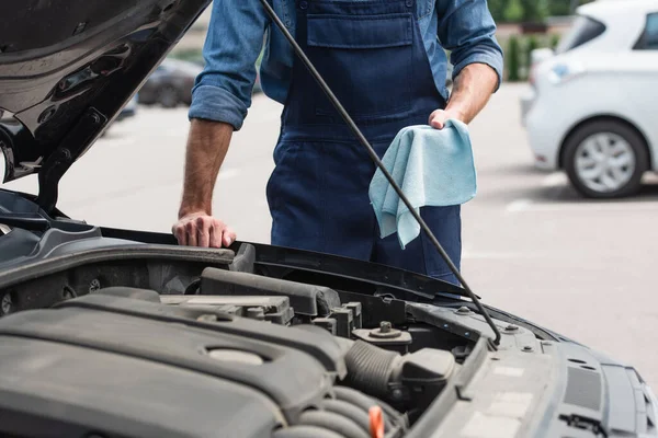 Cropped view of mechanic holding rag near auto with open hood outdoors — Stock Photo