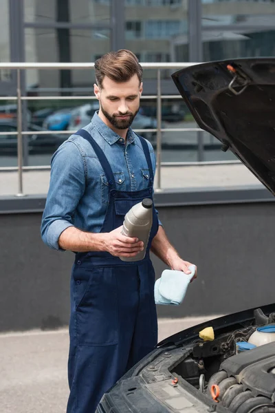 Mécanicien tenant bouteille de vernis et chiffon près de la voiture à l'extérieur — Photo de stock