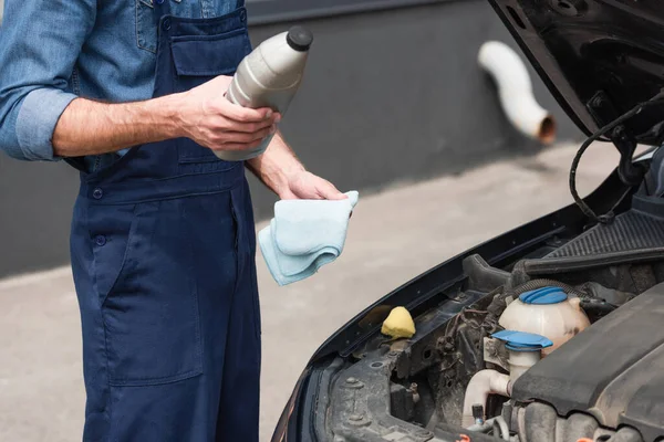 Cropped view of mechanic holding bottle of polish and rag near auto — Stock Photo