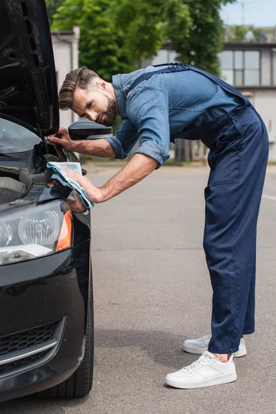 Mechanic in uniform waxing car with rag outdoors — Stock Photo
