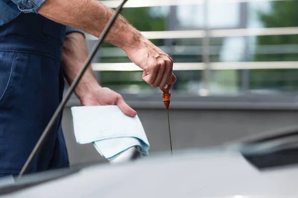 Cropped view of repairman with rag and dipstick checking oil in motor of car — Stock Photo