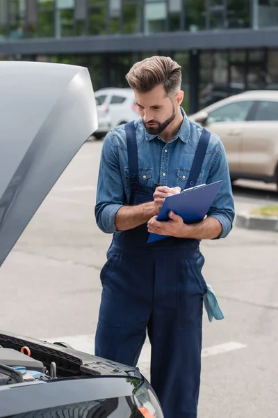 Scrittura meccanica sugli appunti mentre si guarda il motore di auto all'aperto — Foto stock