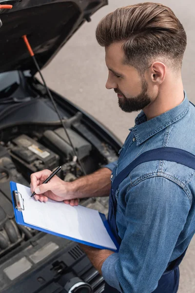 High angle view of mechanic writing on clipboard near blurred car — Stock Photo