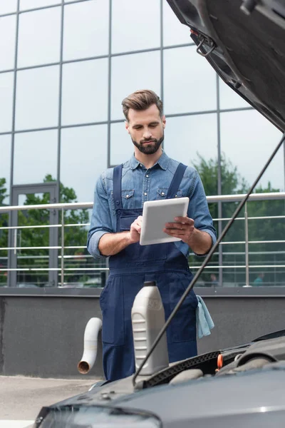 Mechanic using digital tablet near bottle of motor oil on car — Stock Photo