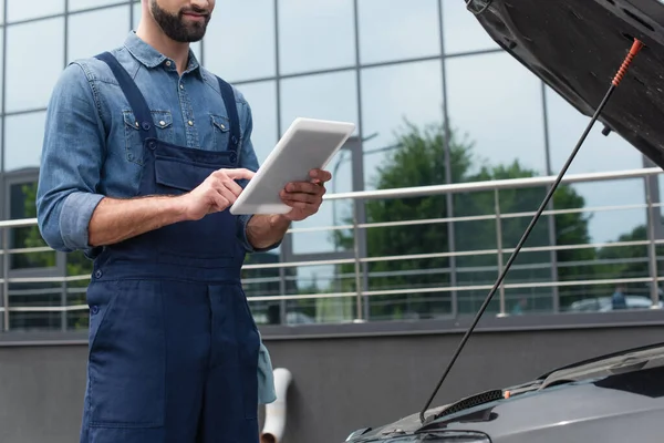 Cropped view of mechanic in overalls using digital tablet near car outdoors — Stock Photo