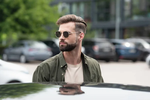 Bearded man in sunglasses standing near blurred car — Stock Photo