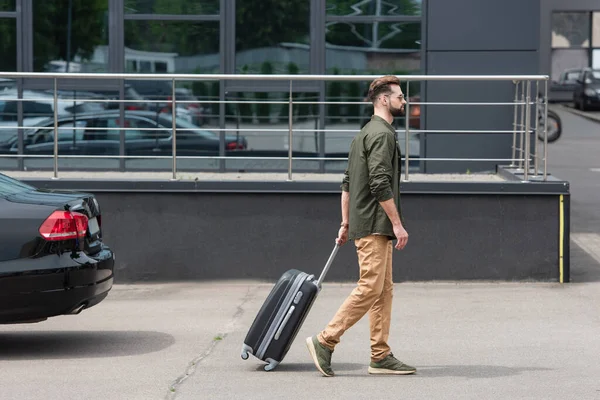 Side view of man with suitcase walking near car outdoors — Stock Photo