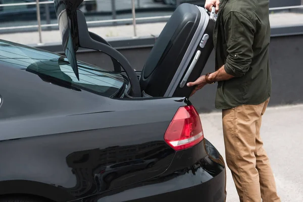 Обрезанный вид человека положить чемодан в багажник автомобиля на открытом воздухе — стоковое фото