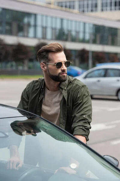 Homme en lunettes de soleil regardant loin près de la voiture à l'extérieur — Photo de stock