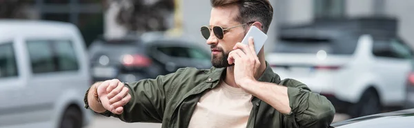 Young man in sunglasses talking on smartphone near top of car, banner — Stock Photo