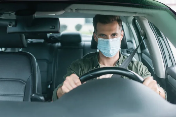 Driver in medical mask looking at camera in auto — Stock Photo
