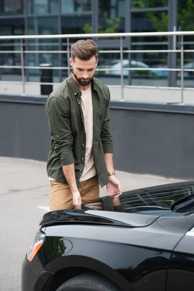 Bearded driver standing near hood of auto outdoors — Stock Photo