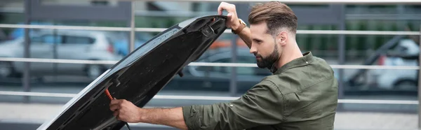 Side view of brunette driver opening car hood outdoors, banner — Stock Photo