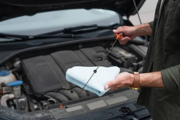 Vista ritagliata del conducente che tiene il bastone e lo straccio mentre controlla l'olio del motore in auto — Foto stock