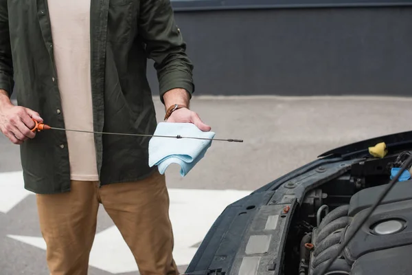 Cropped view of driver holding dipstick and rag near motor of car — Stock Photo