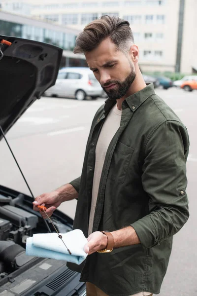 Confused driver checking oil of motor near car outdoors — Stock Photo