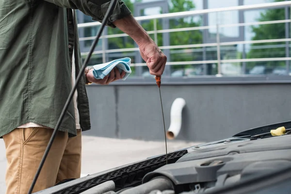 Cropped view of man with rag and dipstick checking oil in engine in car — Stock Photo