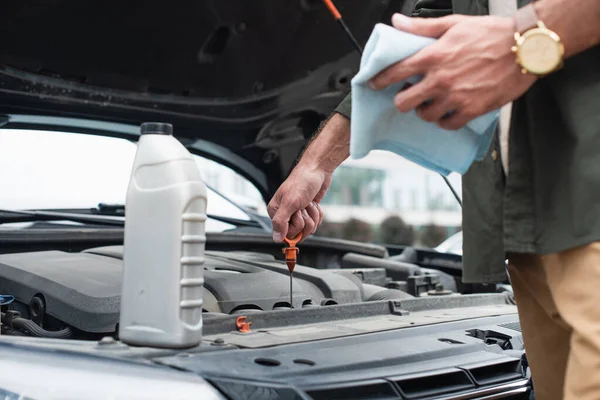 Ausgeschnittene Ansicht eines Mannes, der das Öl des Motors in der Nähe einer Flasche auf einem Auto überprüft — Stockfoto