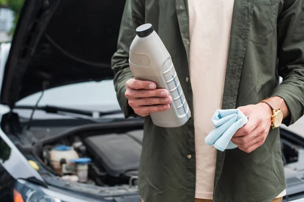 Vue recadrée de l'homme tenant bouteille d'huile moteur et chiffon près de flou auto — Photo de stock