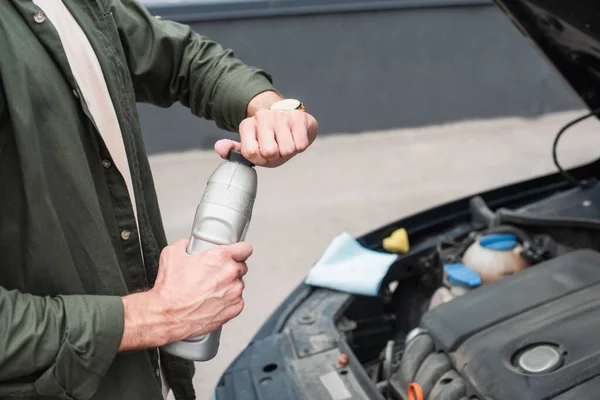 Vista ritagliata del conducente aprendo bottiglia di olio motore vicino auto all'aperto — Foto stock