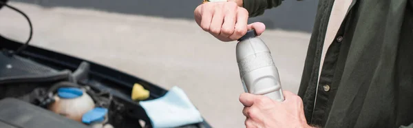 Cropped view of man opening bottle of engine oil near car, banner — Stock Photo