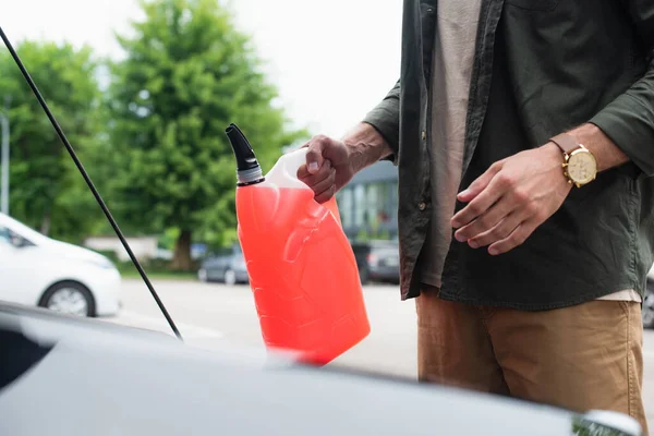 Cropped view of driver holding canister of antifreeze near car — Stock Photo
