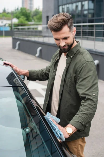 Bearded driver waxing car with rag outdoors — Stock Photo