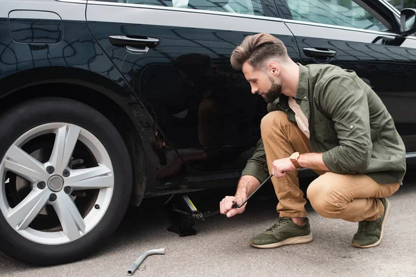 Side view of man using lift jack on car outdoors — Stock Photo